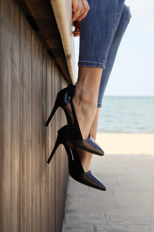 Woman in heels sitting on ledge by the sea